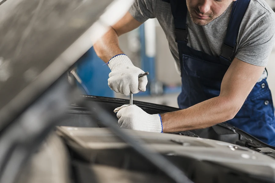 A car mechanic makes an adjustment to an engine using a specialized tool